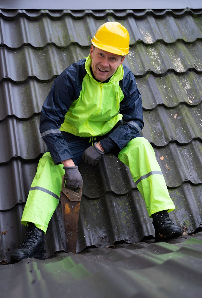 Smiling construction worker wearing safety gear cutting roof tiles with a saw.